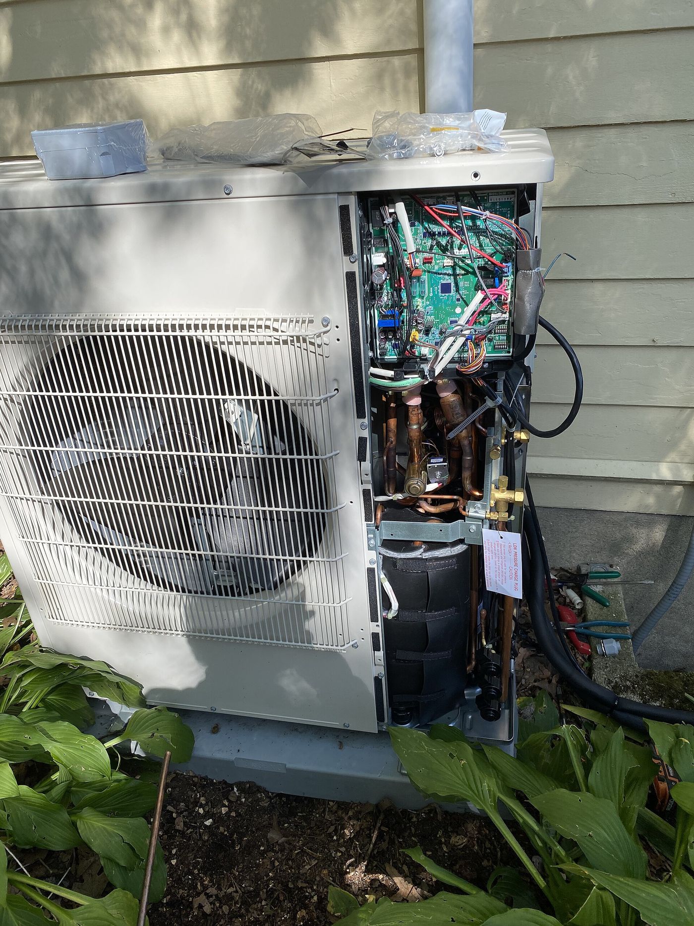 Outdoor heat pump with its cover removed, showing the fan, coil and wiring