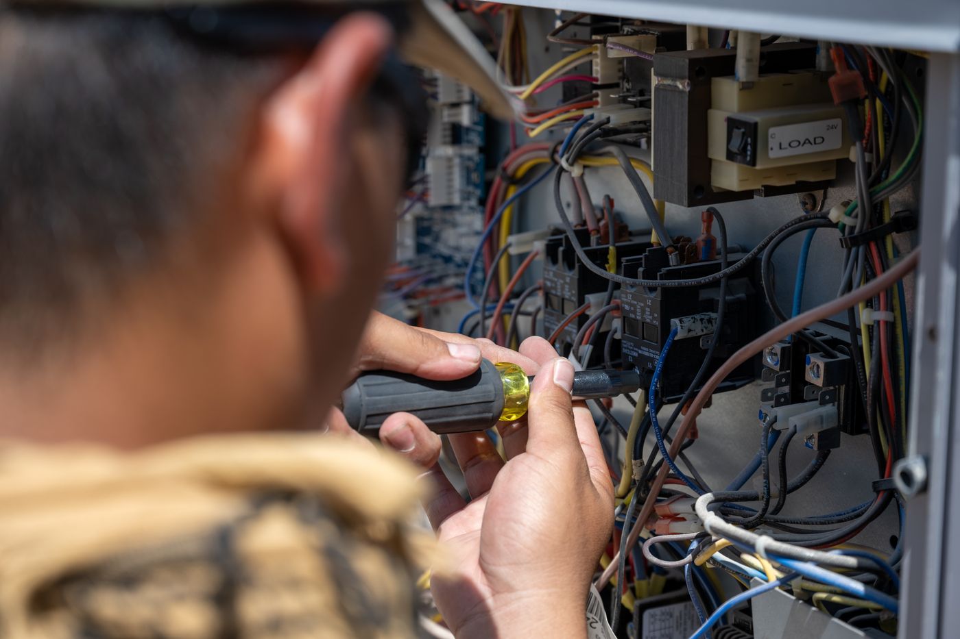 Technician testing wiring inside the control panel of a commercial A/C unit