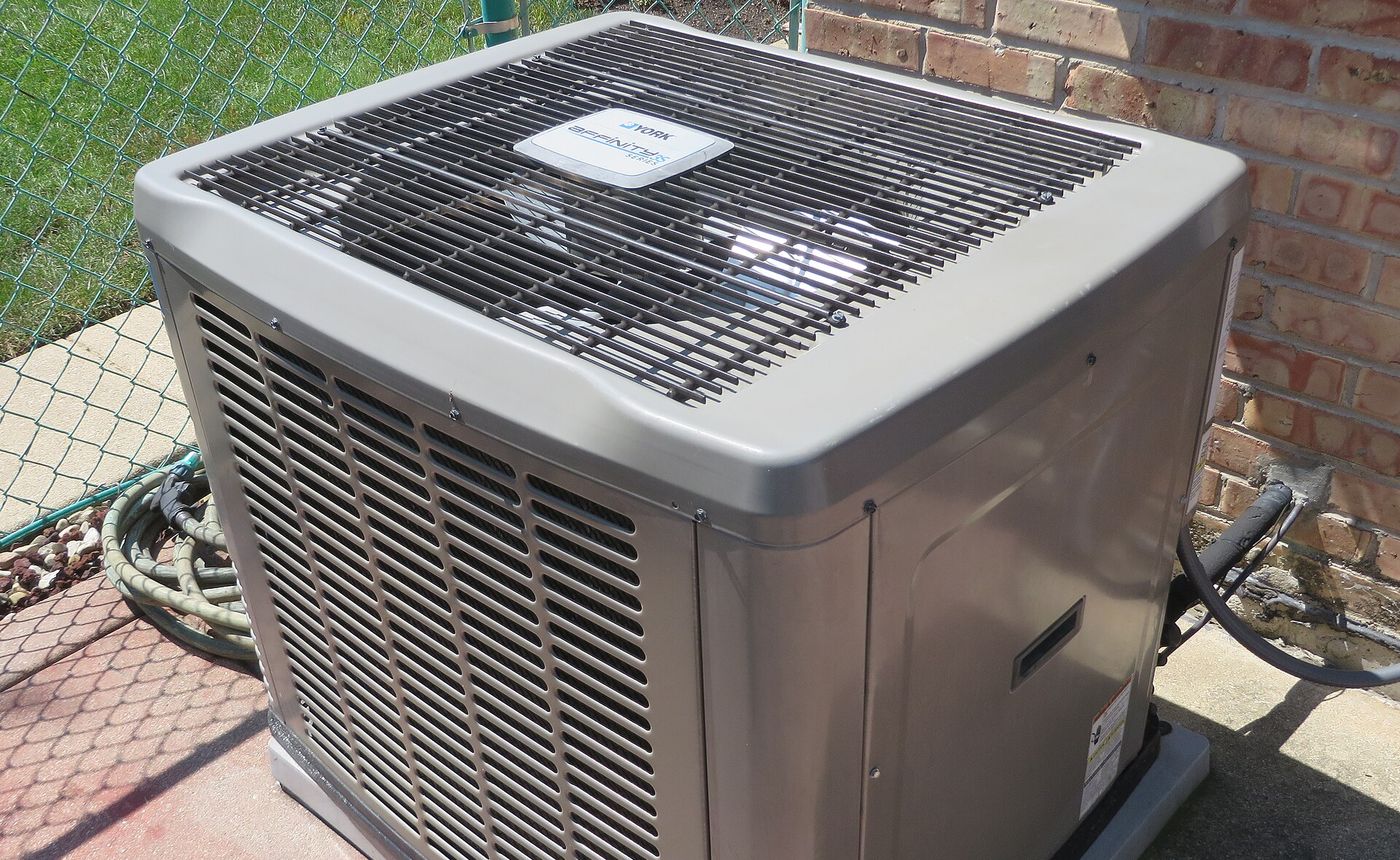 Central air conditioner condenser on a concrete pad beside a brick house