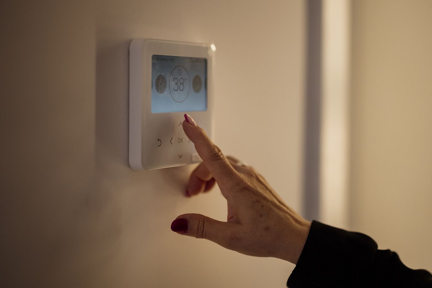 Hand adjusting a digital wall thermostat