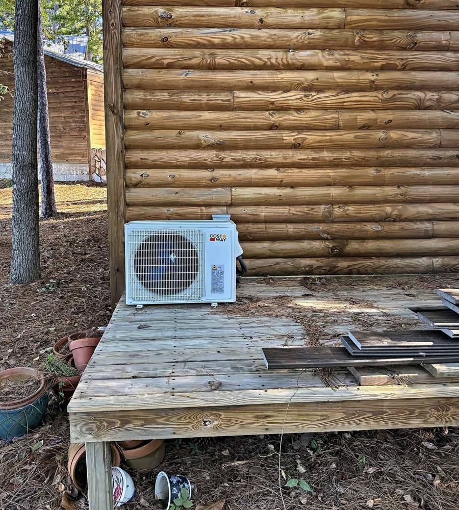 Ductless mini split outdoor unit installed on a wood deck beside a log cabin