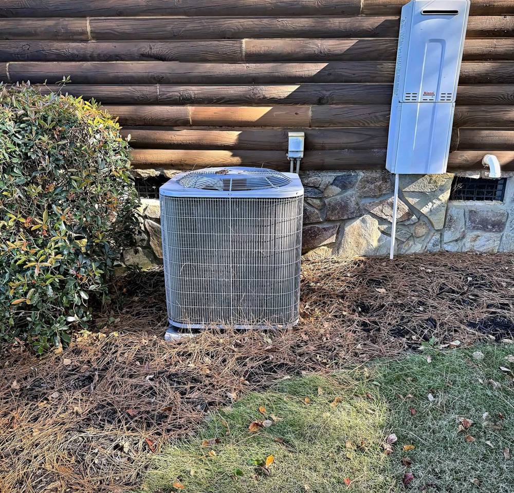 Central air condenser on a pad beside a stone and log home foundation